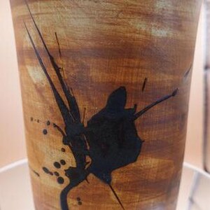 Könnte beinhalten: Eine braune Keramikvase mit schwarzen abstrakten Designs. Die Vase hat eine strukturierte Oberfläche und eine breite Öffnung.