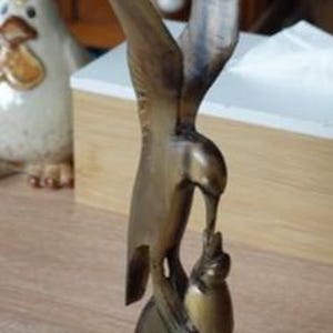 Peut inclure: Sculpture en bois sculpté d'un oiseau de proie, peut-être un aigle ou un faucon, aux ailes déployées. L'oiseau est perché sur une base arrondie, montée sur un bloc de bois rectangulaire. La sculpture a une finition naturelle.