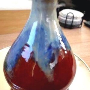 Op de afbeelding: Een handgemaakte keramische vaas met een glanzende afwerking. De vaas heeft een kleurovergang, die overgaat van een dieprode basis naar een blauw-wit bovenstuk. De vaas heeft een bolvormig lichaam en een smalle hals.