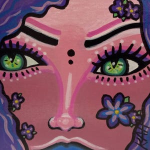 May include: A close-up painting of a face with green eyes, purple hair, and floral accents. The face is painted in shades of pink and purple, with black and white details on the eyebrows and eyelashes. Small purple flowers are placed around the face.