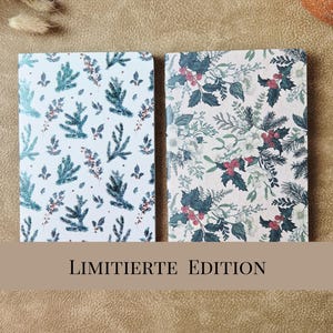 May include: Two rectangular notebooks featuring festive botanical patterns. The left notebook displays a light background with blue-green pine sprigs. The right notebook features a cream background with dark green holly leaves and red berries.