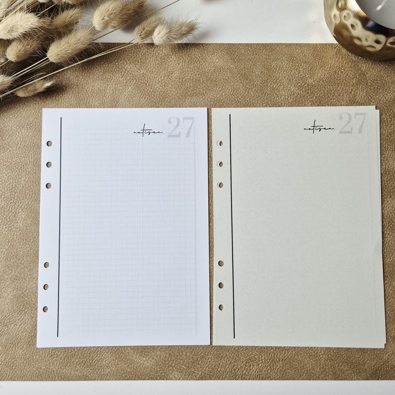 May include: Two rectangular planner refill pages with five punched holes along the left edge. The left page is white with a light gray grid, while the right page is cream-colored. Both feature the text "notizen" and the number "27" at the top.