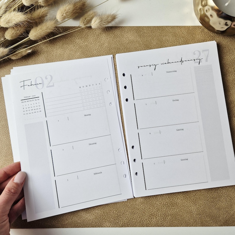 May include: A white paper planner insert with black ink, featuring a monthly calendar for February, a weekly schedule layout with days of the week in German, and punched holes along the side for binding. The pages include grid sections.