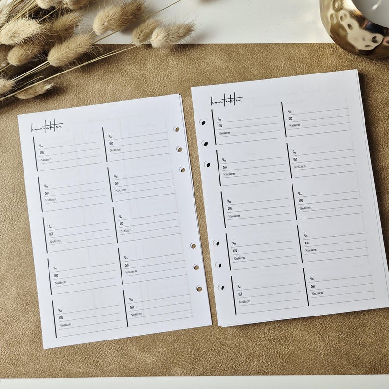 May include: Two white planner insert pages with the word Kontakte printed at the top. Each page features a grid layout with sections for contact information, including icons for phone and email, and a designated space labeled Notizen for notes.