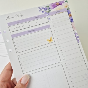 Puede incluir: Una hoja de recambio para agenda diaria con un borde floral de flores moradas y blancas. El diseño incluye secciones para fecha, prioridades, una lista de tareas y un horario de 5 a 21. Un pequeño gráfico de mariposa amarilla está impreso.