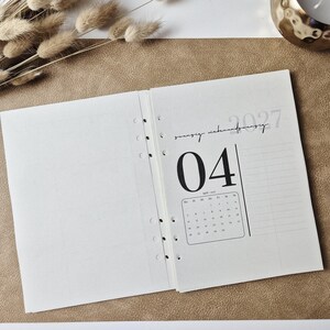 May include: An open planner refill with six ring-binder holes along the center. The right page displays the year 2027, the month April, and a calendar grid for the month. The text 04 is printed in a large font, and the page features a grid layout.