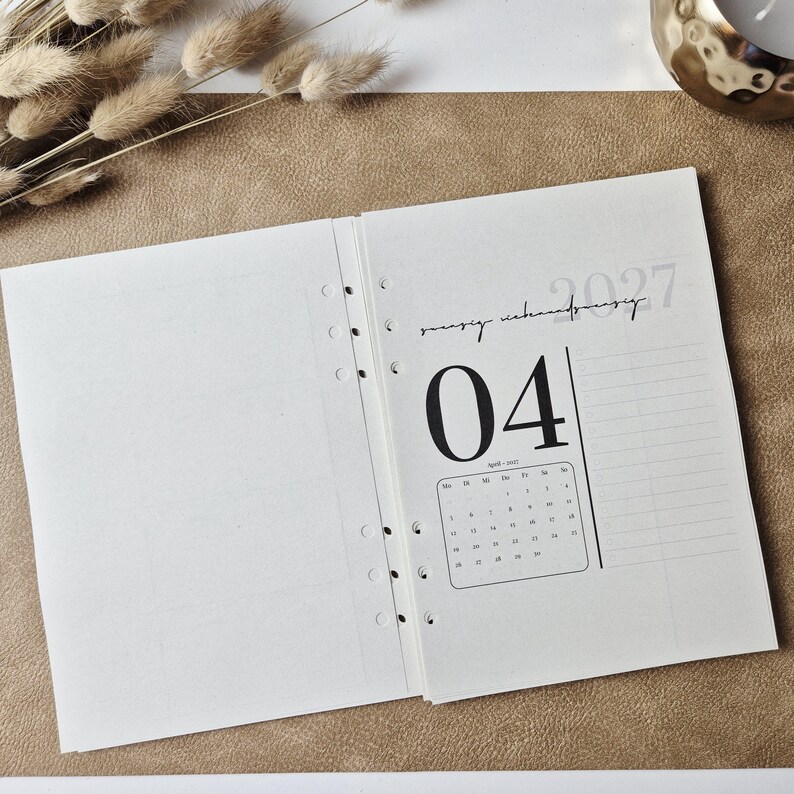 May include: An open planner refill with six ring-binder holes along the center. The right page displays the year 2027, the month April, and a calendar grid for the month. The text 04 is printed in a large font, and the page features a grid layout.