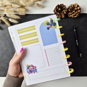 May include: A disc-bound planner insert featuring a white dotted grid page with yellow horizontal bars, a blue arch shape, a pink bulleted list, and illustrations of blackberries, strawberries, and blueberries. The page has colourful plastic discs.