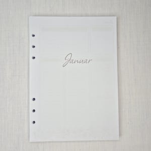 May include: A white planner page with the word "Januar" in a cursive font. The page has a grid layout with sections for notes and scheduling. The page has several holes on the left side for binding.