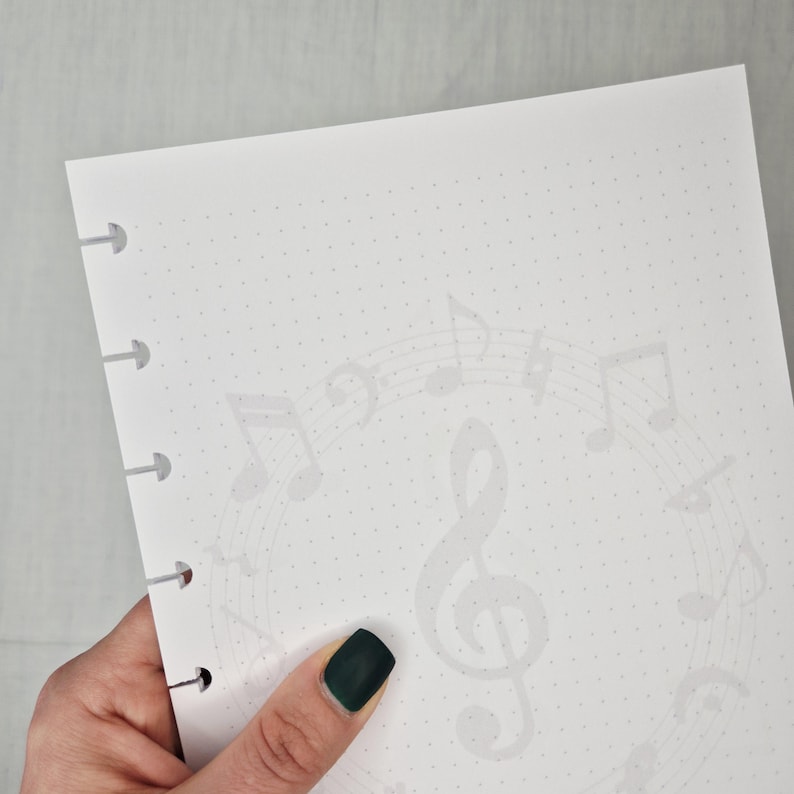 May include: White dot-grid paper with a musical theme. A faint circular pattern of musical notes and a treble clef decorates the paper. The paper has holes along the left edge, with arrows pointing to them.