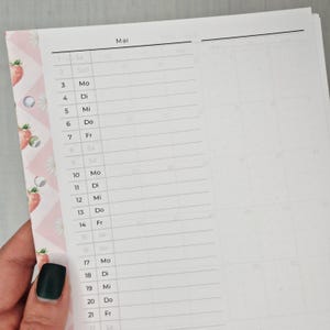 May include: A partially visible planner page with the month of May. The left side has a pink border with strawberry and daisy patterns. The page is divided into days of the week with lines for notes. The word "Mai" is at the top.