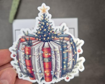 May include: A sticker featuring a stack of open books decorated as a Christmas ornament. A Christmas tree sits atop the books, adorned with a star, lights, and ornaments. The books have red, blue, and gold spines.