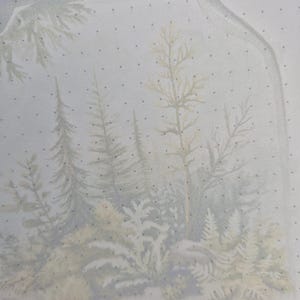 May include: A jar-shaped illustration with a forest scene inside. The artwork features various trees, ferns, and foliage in muted green, beige, and gray tones. The background is a light blue with small black dots.