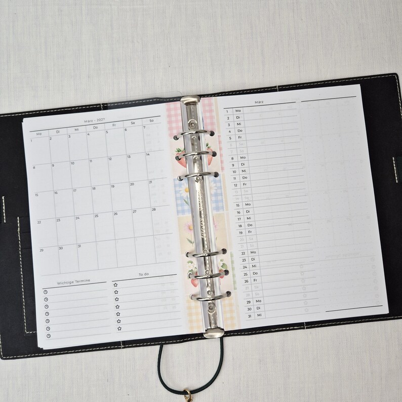 May include: Open black leather binder with a calendar and daily planner pages. The calendar shows the month of March 2021. The planner pages have a floral design and a to-do list.