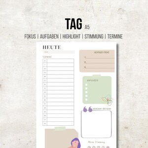 Può includere: Pagina di pianificazione giornaliera in formato A5 con la parola "TAG" in alto. La pagina include sezioni per "FOKUS", "AUFGABEN", "HIGHLIGHT", "STIMMUNG" e "TERMINE". Offre spazi per la pianificazione, le attività e il monitoraggio dell'umore.