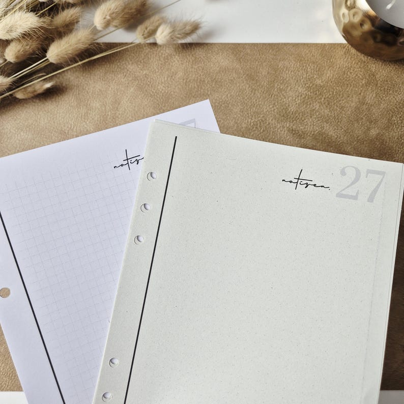 May include: Two white planner refill pages with pre-punched holes along the left side. The top page is light gray with the text "notizen" and the number "27" in the corner. The bottom page features a grid pattern and the text "notizen".