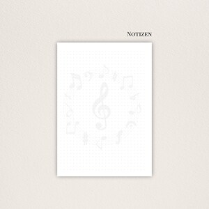 May include: A white notepad featuring a dotted grid and light grey musical notes. The word "NOTIZEN" is printed at the top. The musical notes include treble clefs and other musical symbols.