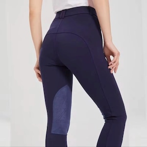 May include: Navy blue riding breeches with a high waist and a dark blue suede knee patch. The breeches have a tailored fit and a belt loop waistband. The image shows the back of the breeches.