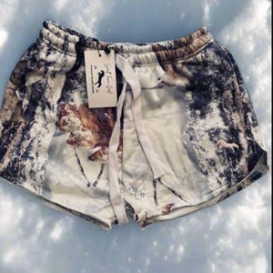 Puede incluir: Shorts de algod&oacute;n blanco con estampado de bosque que incluye &aacute;rboles, nieve y ciervos. Los shorts tienen cintura con cord&oacute;n y una etiqueta que dice "Small Town Girl" con un logotipo de caballo.