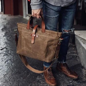Peut inclure: Un sac fourre-tout en toile marron avec des sangles en cuir et une longue bandoulière. Le sac a une fermeture éclair et un rabat avec une boucle.