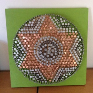 May include: A circular nail art piece with a copper, silver, and white design on a green square background. The nails are arranged in concentric circles, creating a textured, eye-catching pattern. The artwork is mounted on a green square.
