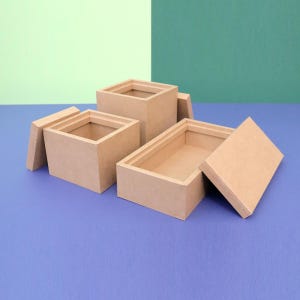 Pode incluir: Três caixas retangulares abertas, castanho claro, com tampas. As caixas estão dispostas sobre uma superfície azul com um fundo verde e verde claro. As caixas são feitas de um material resistente.