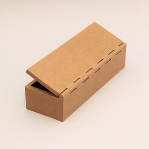 May include: A light brown rectangular cardboard box with a hinged lid, partially open. The box's lid is attached with a series of folded cardboard tabs. The interior of the box is visible.