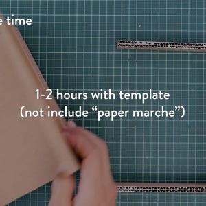 May include: A craft project in progress, featuring a brown cardboard frame and a folded piece of cardboard. The text indicates an estimated completion time of 1-2 hours with a template, excluding paper mache. The background is a green cutting mat.