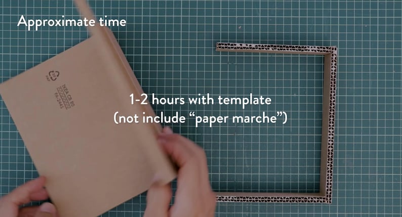 May include: A craft project in progress, featuring a brown cardboard frame and a folded piece of cardboard. The text indicates an estimated completion time of 1-2 hours with a template, excluding paper mache. The background is a green cutting mat.