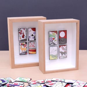May include: Two framed art pieces with miniature Japanese-style illustrations. Each frame is a light brown color and contains six small, colorful images. The illustrations depict various scenes, including figures, animals, and floral patterns.