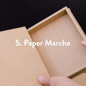 May include: A rectangular, open paper mache box with a lid. The box is light brown and the text "5. Paper Marche" is visible on the image. The box is being held open by a person.
