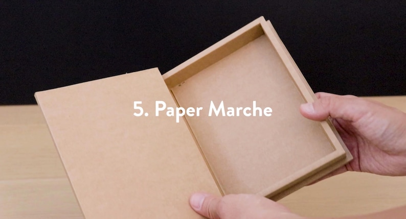 May include: A rectangular, open paper mache box with a lid. The box is light brown and the text "5. Paper Marche" is visible on the image. The box is being held open by a person.