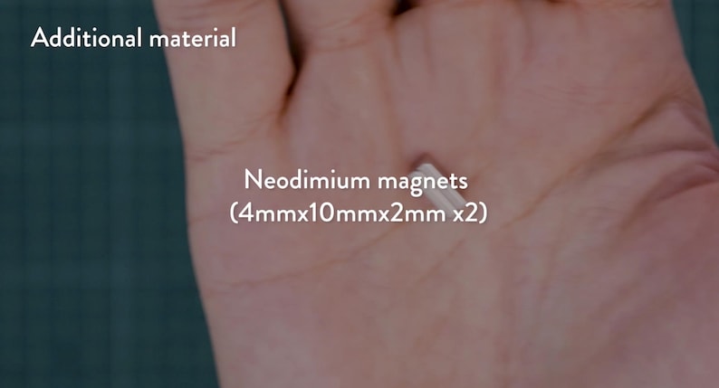 May include: A close-up of a hand holding two small, rectangular neodymium magnets. The magnets are silver and measure 4mm x 10mm x 2mm each. Text in the image reads "Neodimium magnets (4mmx10mmx2mm x2)" and "Additional material".