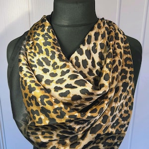May include: A black and gold leopard print silk scarf. The scarf is draped around a black mannequin.