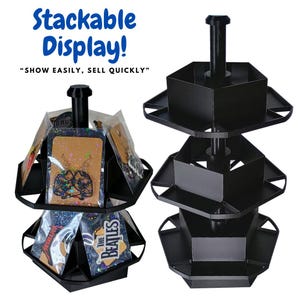 Può includere: Espositore impilabile nero con più livelli, che mostra orecchini confezionati e altri piccoli oggetti. Il display ha un palo centrale e ripiani angolati. Il testo recita "Stackable Display!" e "SHOW EASILY, SELL QUICKLY".