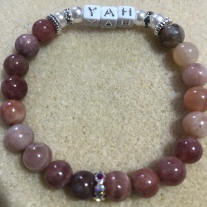 Op de afbeelding: Een roze en oranje sunstone kralen armband met een zilveren bedel waarop in witte letters "YAH" staat. De armband heeft een kleine zilveren kraal met een heldere strass in het midden.