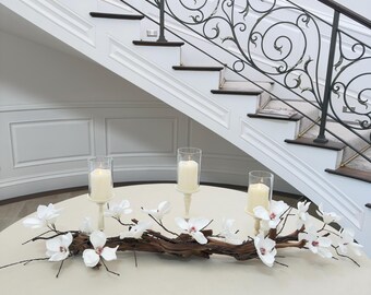 Centro de mesa de comedor con madera flotante: flores de magnolia, candelabros color marfil y velas sin llama.