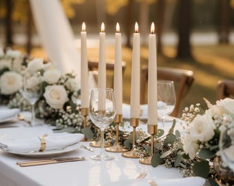 May include: Elegant table setting with lit candles, white roses, and gold accents. The table is set with white plates, napkins, and gold cutlery. Wine glasses and floral arrangements complete the sophisticated look, perfect for a wedding or special event.