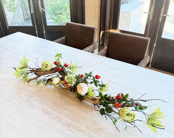 Centro de mesa de granada con tallos de manzana y peonías para decorar la mesa del comedor.