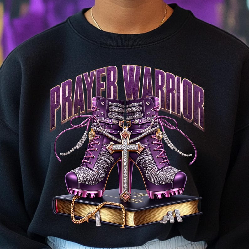 May include: A black sweatshirt with the words "PRAYER WARRIOR" in gold lettering. The design features a pair of purple high-heeled shoes with rhinestones, a gold cross, and a gold chain on a bible.