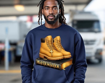 May include: Navy blue sweatshirt with a graphic of tan work boots and a gold cross pendant, placed on a black book with the words "PRAYER WARRIOR" in gold. The sweatshirt has a front pocket and a crew neck.