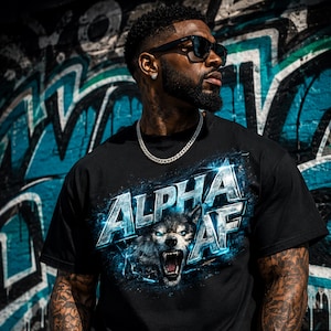 May include: Black t-shirt with the text "ALPHA AF" and a wolf graphic. The wolf has blue eyes and is snarling. The shirt is worn by a person wearing sunglasses and a silver chain necklace.
