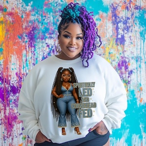 Puede incluir: Sudadera blanca con una ilustración de dibujos animados de una mujer negra con trenzas largas que lleva un atuendo vaquero. El texto "Spiritually Led and Cornbread Fed" está impreso en la sudadera.