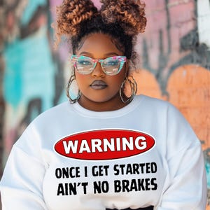 May include: White sweatshirt with a red oval warning sign that says "WARNING ONCE I GET STARTED AIN'T NO BRAKES".