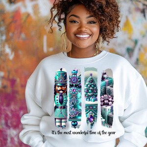 May include: White sweatshirt with a Christmas-themed design featuring a nutcracker, a Christmas tree, and presents. The design is in shades of teal, purple, and gold. The text "it's the most wonderful time of the year" is printed below the design.