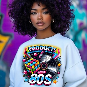 May include: A white sweatshirt with a colorful graphic design featuring the text "Products of the 80s" with a Rubik's Cube, a vinyl record, and stars.