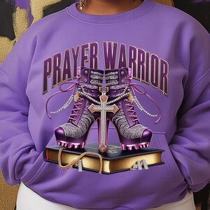 May include: Purple sweatshirt with the text "PRAYER WARRIOR" in gold lettering. The sweatshirt features a pair of purple high-heeled boots with rhinestones and a gold cross.