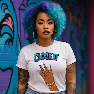 May include: White t-shirt with the text "CLOCK IT" in a blue and purple bubble font. The shirt features a graphic of a brown hand with long, teal and purple fingernails, and a gold bracelet. The background is a colorful graffiti wall.