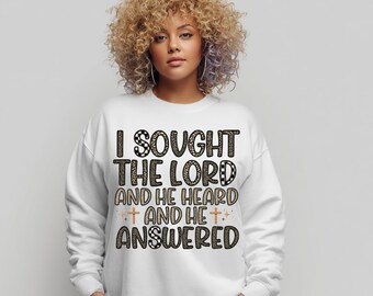 Puede incluir: Sudadera blanca con el texto "I SOUGHT THE LORD AND HE HEARD AND HE ANSWERED" en una mezcla de estampado de leopardo y letras color beige. La sudadera tiene cuello redondo y mangas largas.