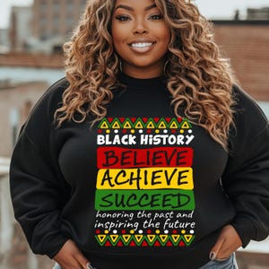 Pode incluir: Camisola de moletom preta com um design gráfico colorido que diz "Black History Believe Achieve Succeed honoring the past and inspiring the future".